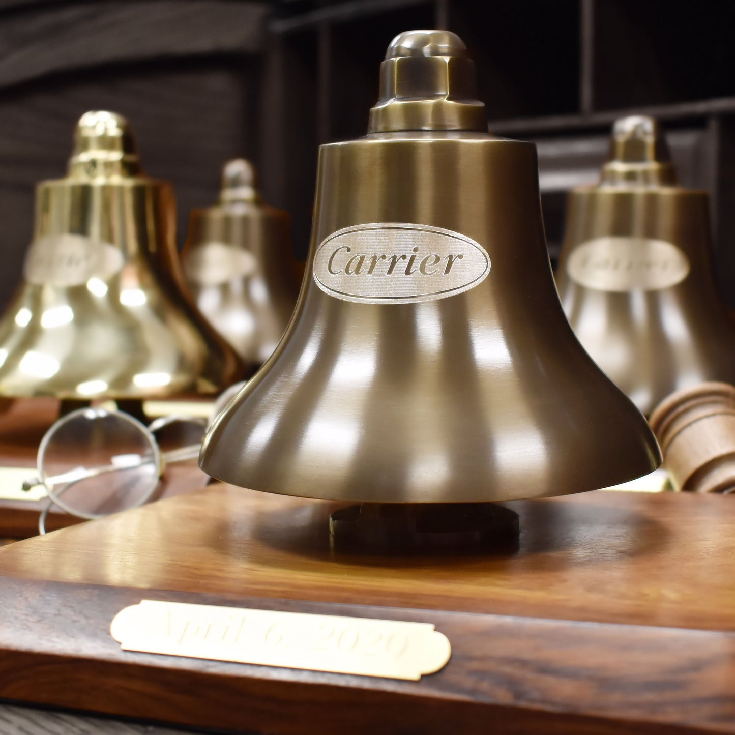 Bronze bell with 'Carrier' engraving on a wooden base, surrounded by similar bells.